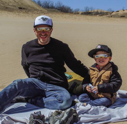 Jeremiah (left) and Elijah (right) Barker enjoy what will most likely be the only solar eclipse the father and son will see together at the Dune Climb on Monday. The father and son duo, like many, brought glasses, snack, and blankets to enjoy the celestial spectacle. Enterprise photo by Brian Freiberger